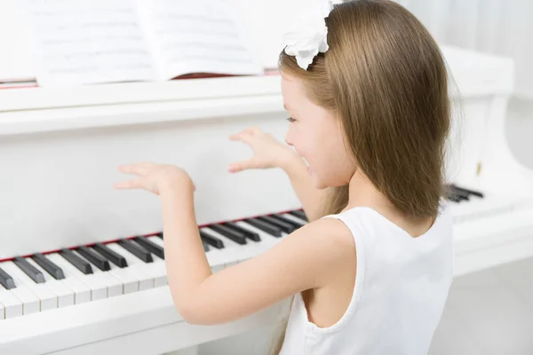 Bakifrån av liten flicka i vit klänning spela piano — Stockfoto