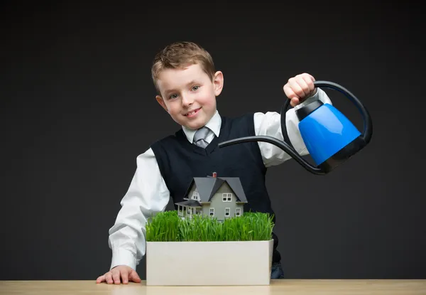 Ragazzino versando modello di casa e erba verde — Foto Stock