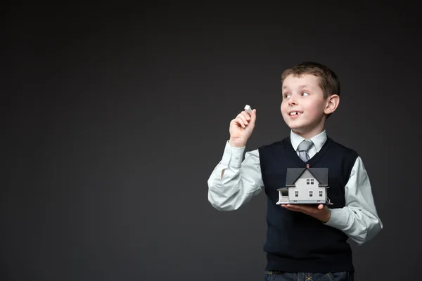 Mały chłopiec pisania kredą i utrzymanie domu modelu — Zdjęcie stockowe