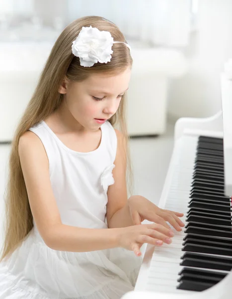 Портрет маленького ребенка в белом платье, играющего на пианино — стоковое фото