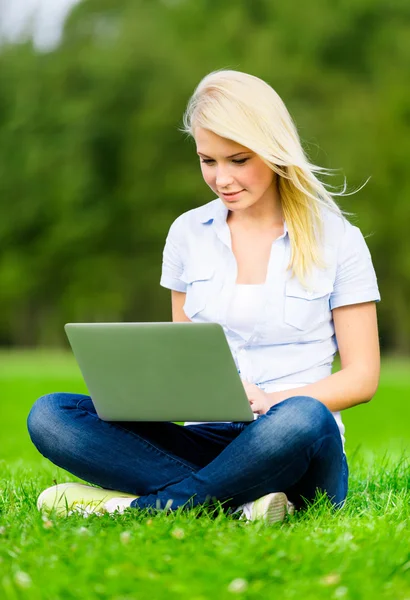 Девушка с ноутбуком сидит на зеленой траве — стоковое фото