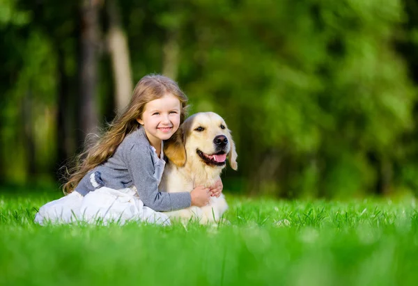 Liten flicka sitter på gräset med golden retriever — Stockfoto