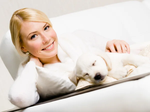 Uyuyan bir köpek yavrusu ile kanepede oturan kadın — Stok fotoğraf