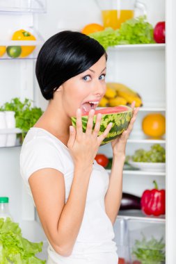 kadın açılan buzdolabının yanında karpuz yiyor