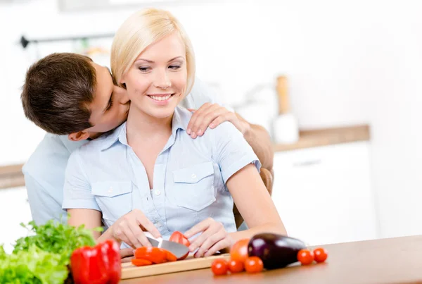 Homem beija mulher bonita enquanto ela está cozinhando — Fotografia de Stock