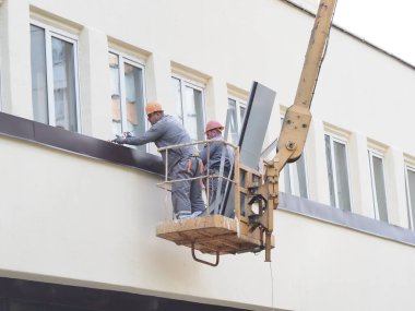 Belarus, Minsk, 2021 inşaat işçileri hidrolik asansörde tulum ve boyalar bir binanın duvarının camını onarıyor.