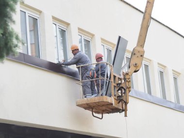 Belarus, Minsk, 2021 inşaat işçileri hidrolik asansörde tulum ve boyalar bir binanın duvarının camını onarıyor.