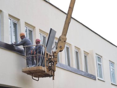 Belarus, Minsk, 2021 inşaat işçileri hidrolik asansörde tulum ve boyalar bir binanın duvarının camını onarıyor.