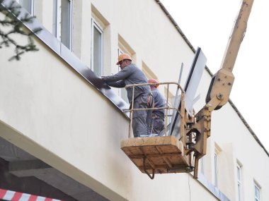 Belarus, Minsk, 2021 inşaat işçileri hidrolik asansörde tulum ve boyalar bir binanın duvarının camını onarıyor.