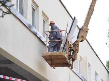 Belarus, Minsk, 2021 inşaat işçileri hidrolik asansörde tulum ve boyalar bir binanın duvarının camını onarıyor.