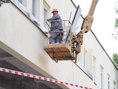 Belarus, Minsk, 2021 inşaat işçileri hidrolik asansörde tulum ve boyalar bir binanın duvarının camını onarıyor.