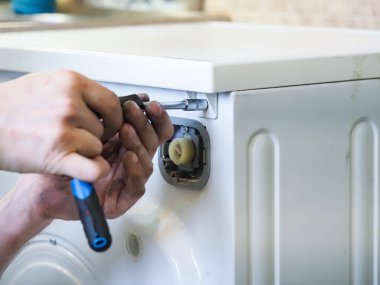 Usta servis elemanı çamaşır makinesini tamir eder.