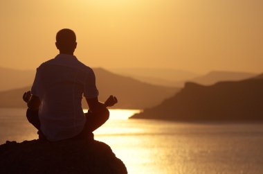 Guy meditating at sunset clipart