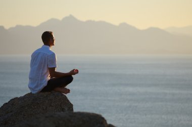 lotus pozisyonunda bir kayaya oturan adam