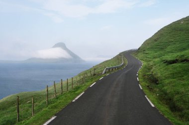 Faroe Adaları 'ndaki Koltur adasına bakan yeşil bir tepenin kenarındaki yol.