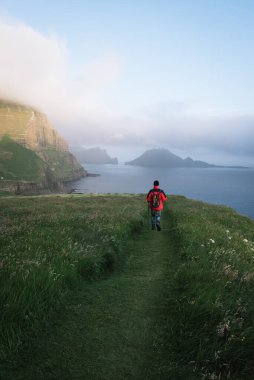Faroe Adaları 'ndaki Gasadalur köyünde yürüyüş. Sırt çantalı bir turist Vagar adasında yol boyunca yürüyor.