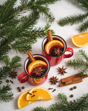 Köknar, portakal ve baharatlardan oluşan dallarla çevrili bir Noel masasında iki kırmızı bardakta sıcak şarap.