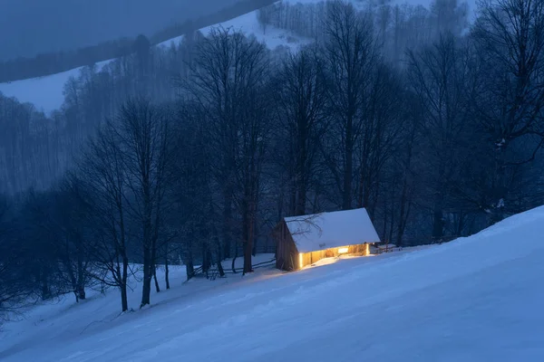 美丽的冬季风景 山上有一个雪屋 晚上从窗户发出温暖的光芒 — 图库照片