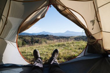 The guy contemplates the view of the mountains from a tourist tent in a mountain hike