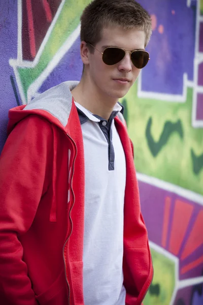 Style teen in glasses standing near graffiti wall. — Stock Photo, Image