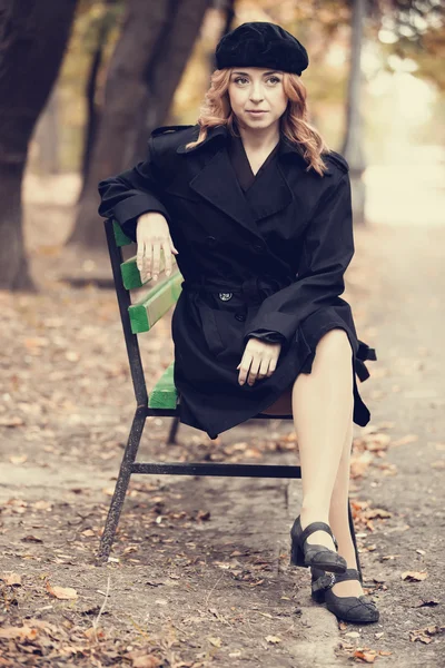 Style redhead girl sitting at bench in autumn park. — Stock Photo, Image