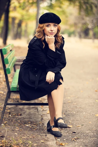 Rotschopf-Mädchen sitzt auf Bank im Herbst-Park. — Stockfoto