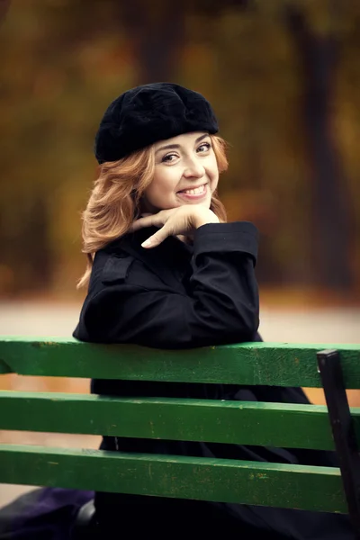 Chica pelirroja estilo sentado en el banco en el parque de otoño . — Foto de Stock