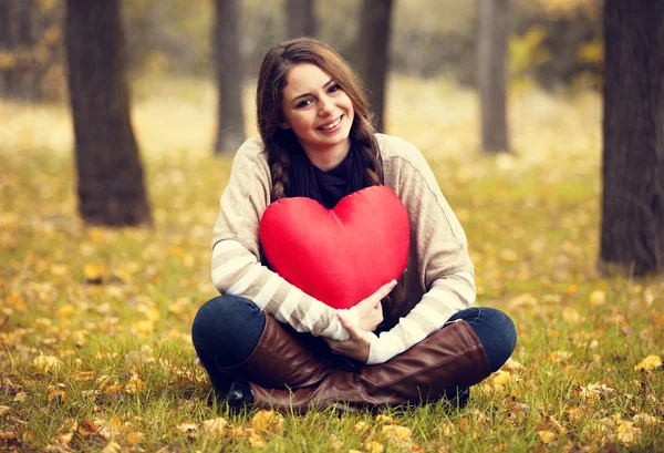 Redhead girl with toy heart at autumn park. Stock Picture