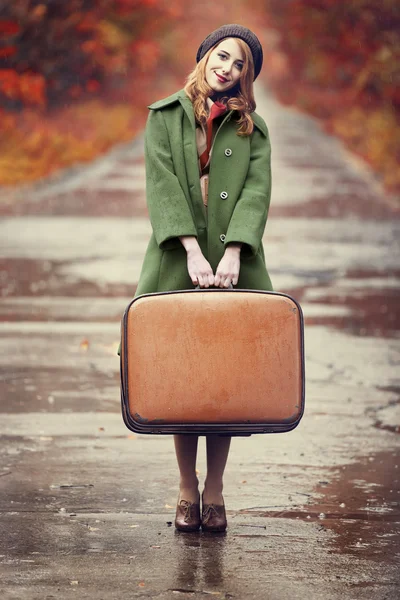 Стильная рыжая девушка с чемоданом в красивом осеннем переулке . — стоковое фото