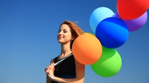 Rödhårig tjej med färg ballonger på blå himmel bakgrund. — Stockvideo