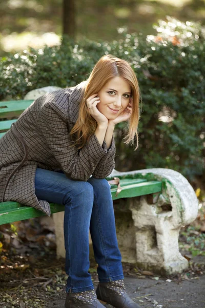 Lächelndes rothaariges Mädchen sitzt auf der Bank. — Stockfoto