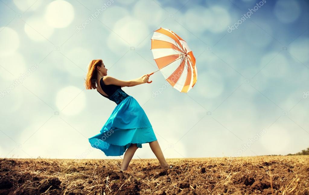 Redhead girl with umbrella at windy field.