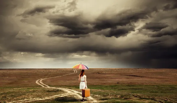 Girl with umbrella and suitcase walking by the road at countrysi — Stock Photo, Image