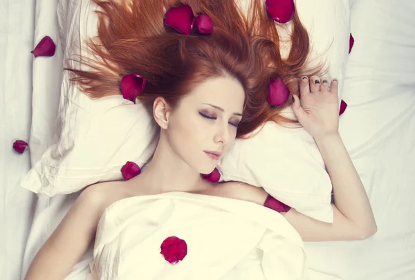 Mooi roodharig meisje in bed met roos bloemblad. studio opname. — Stockfoto
