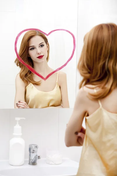 Rotschopf Mädchen in der Nähe Spiegel mit Herz es im Badezimmer. — Stockfoto