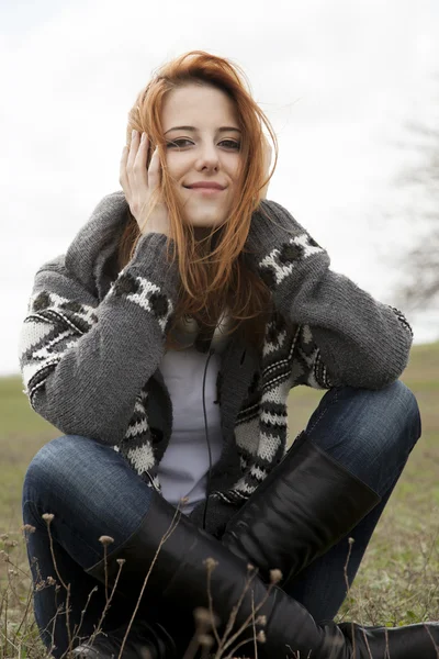 春の牧草地で座っているヘッドフォンで若い女の子. — ストック写真