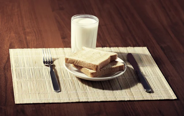 ขนมปังปิ้งกับแก้วนมและมีดบนพื้นหลังไม้ — ภาพถ่ายสต็อก