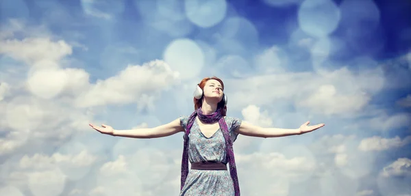 Молодая улыбающаяся девушка в наушниках на фоне голубого неба — стоковое фото