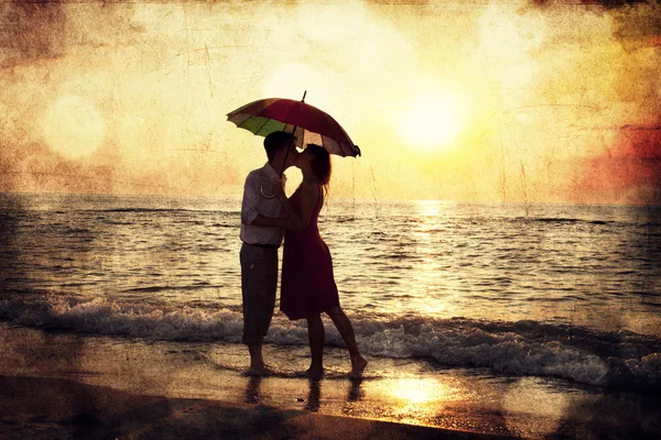 Couple kissing under umbrella at the beach in sunset. Photo in o — Stock Photo, Image