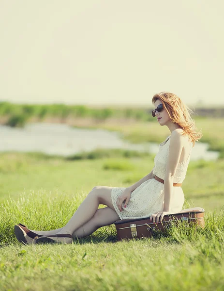 Молода дівчина моди з валізою сидить на весняній траві біля ла — стокове фото