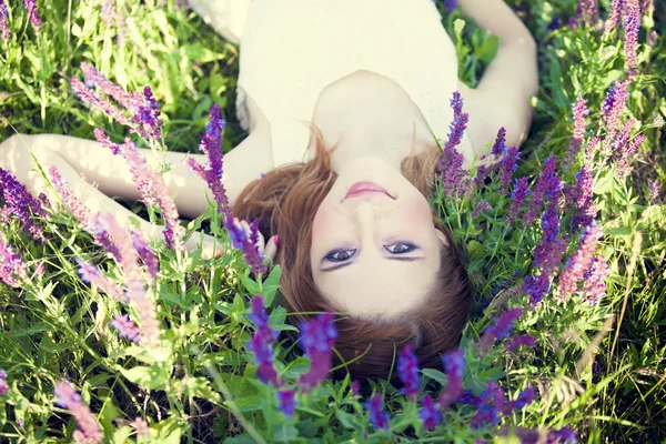 Meisje liyng op lente gras en bloemen. — Stockfoto