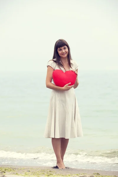 Morena menina segurando brinquedo coração na praia . — Fotografia de Stock