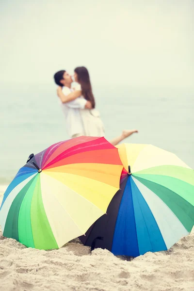 Pareja besándose en la playa con sombrilla — Foto de Stock