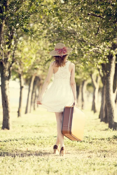 Rusovláska dívka s kufrem v stromu alley. — Stock fotografie