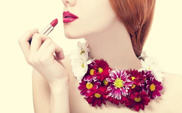 Hermosa pelirroja con flores sosteniendo lápiz labial — Foto de Stock