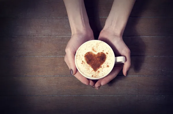 Mulher segurando xícara quente de café, com forma de coração — Fotografia de Stock