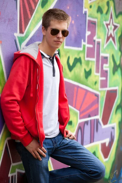 Style teen in glasses standing near graffiti wall. — Stock Photo, Image