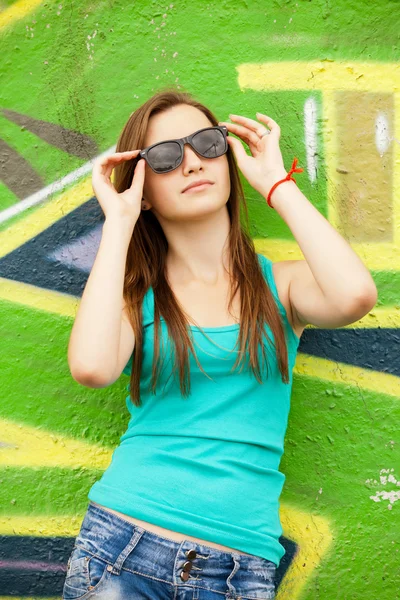 Teenager-Mädchen mit Sonnenbrille in der Nähe von Graffiti-Hintergrund. — Stockfoto