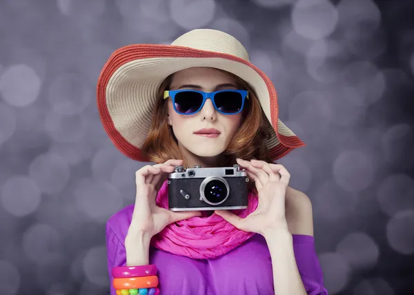 Divertente rossa ragazza in cappello con fotocamera e bokeh sullo sfondo — Foto Stock