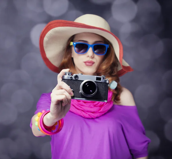 Смешная рыжая девушка в шляпе с камерой и боке на заднем плане — стоковое фото